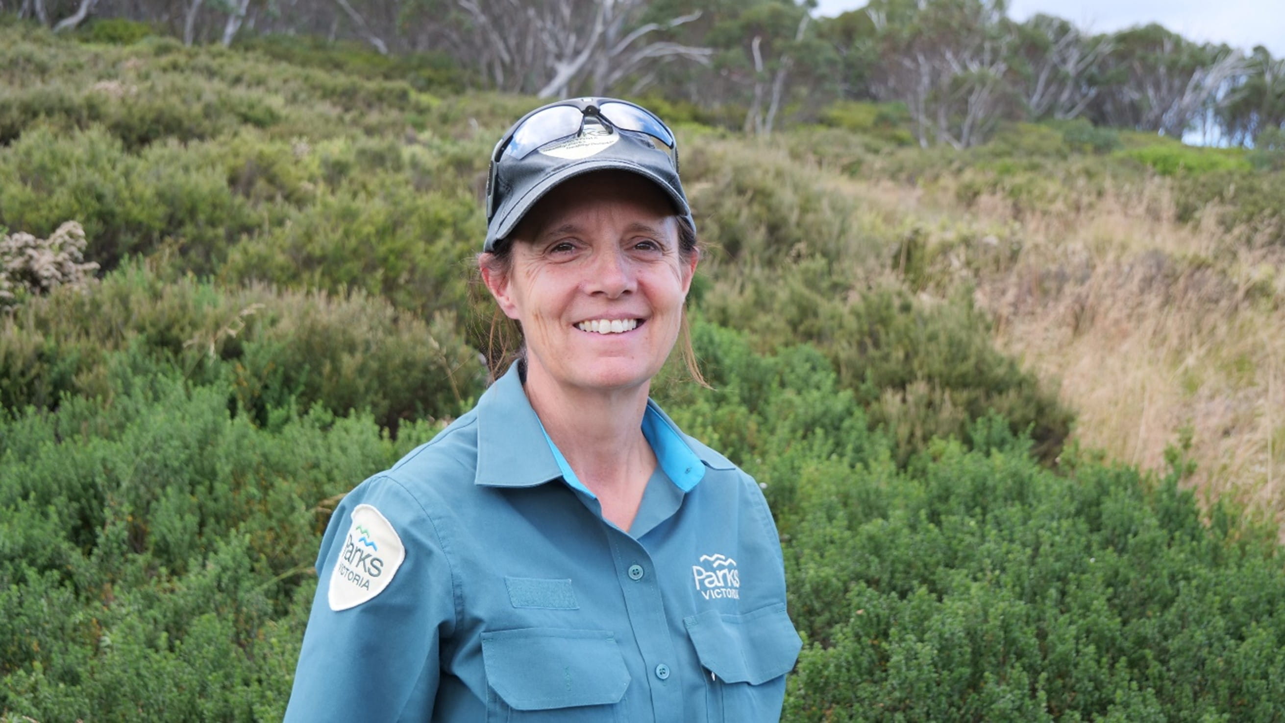 Elaine Thomas, in a dark green uniform, stands in front of green vegetation.