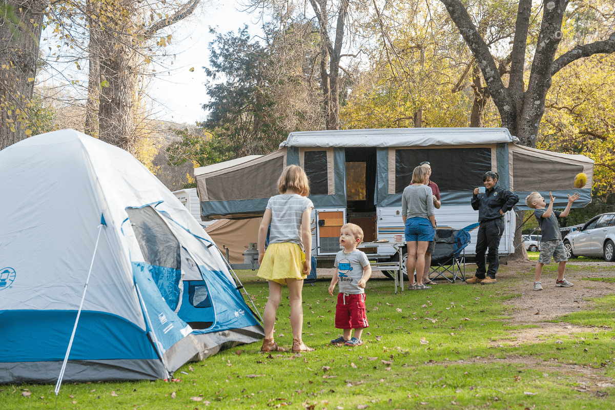 Children and adults talking to each other next to tent and caravan in a campground