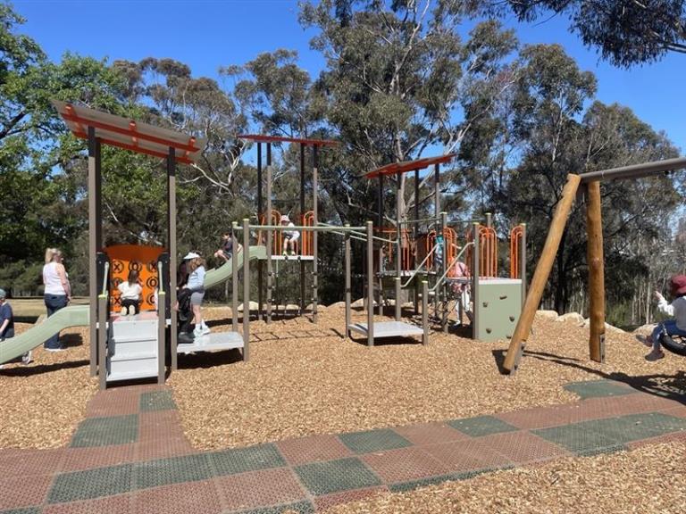 Children and adults playing on the new playground. Blue sky and eucapypts in the background.