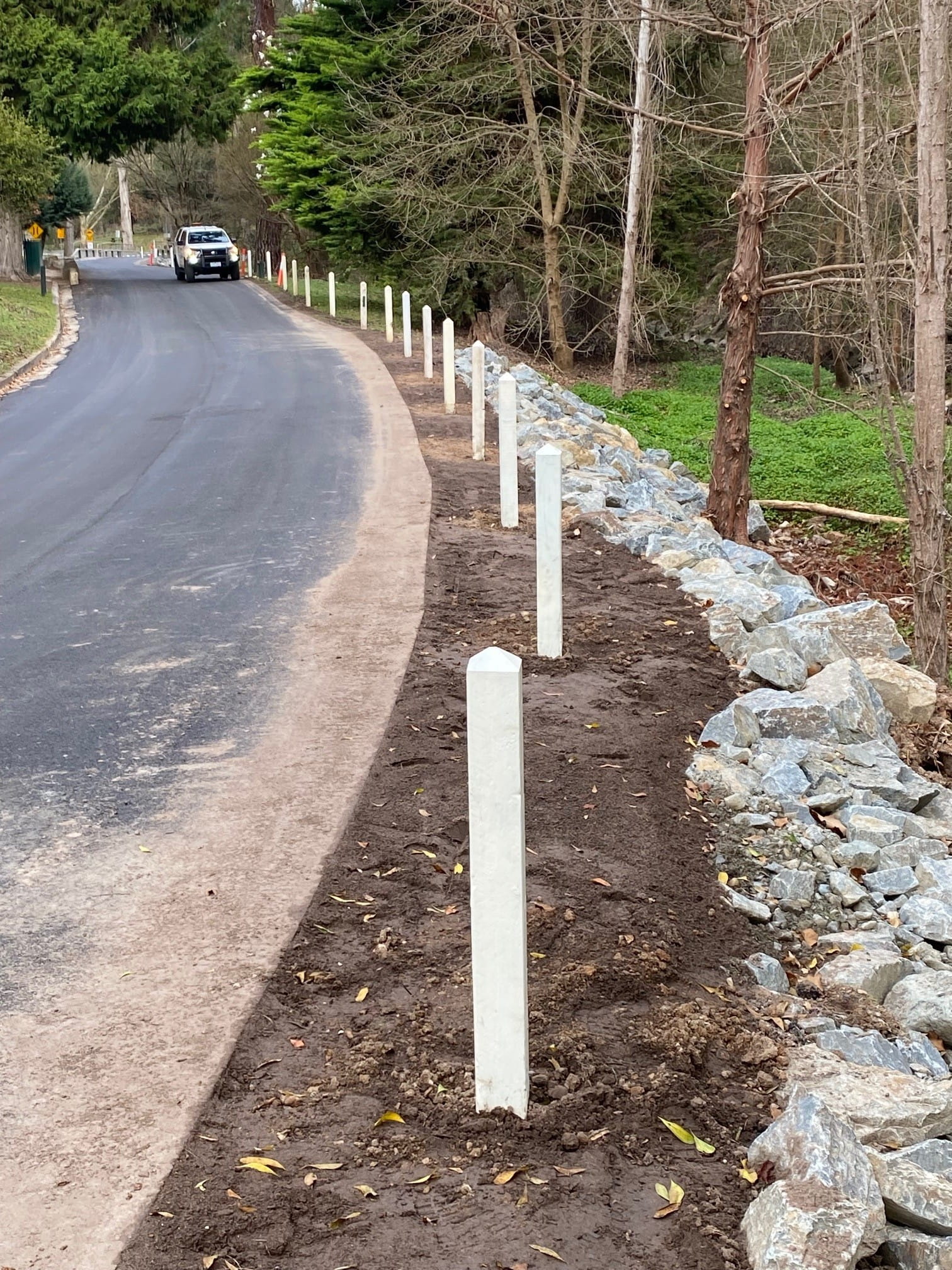New bollards and rocks are installed along the boundary of an asphalt road.