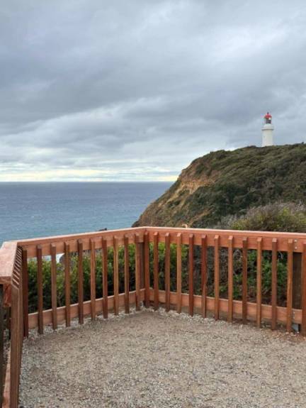 A wooden fence around a lookout point with a view of the ocean and a lighthouse. 