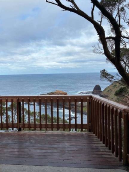 A wooden fence surrounding a lookout platform with a view of the ocean and trees in the background. 