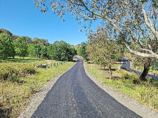 New asphalt access road, sunny day with trees and grass on each side of the road
