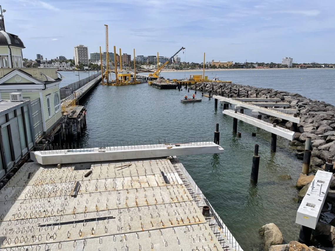 St Kilda pier under construction - cranes, piles of materials and construction fencing and signage is dotted through the structure of the pier. 