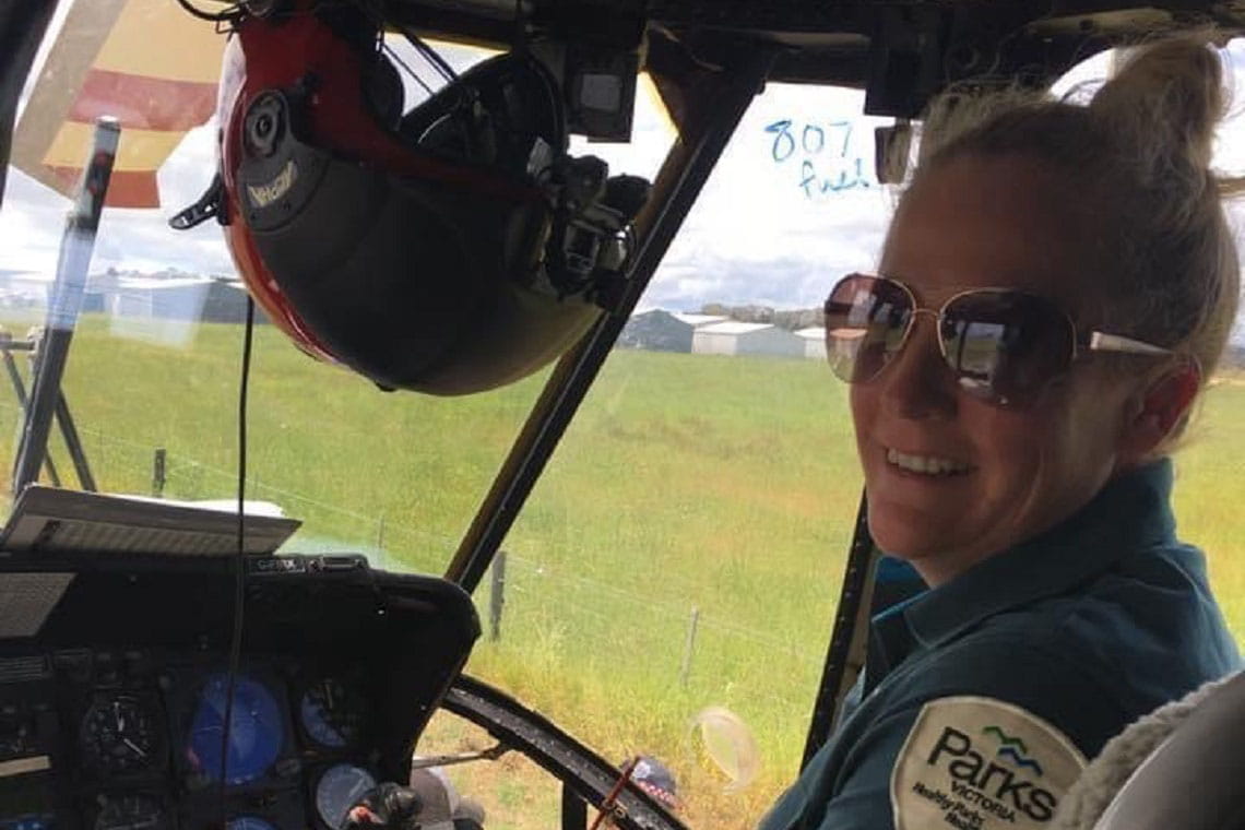 Rhianna sits smiling in the cockpit of a helicopter, wearing her Parks Victoria uniform.