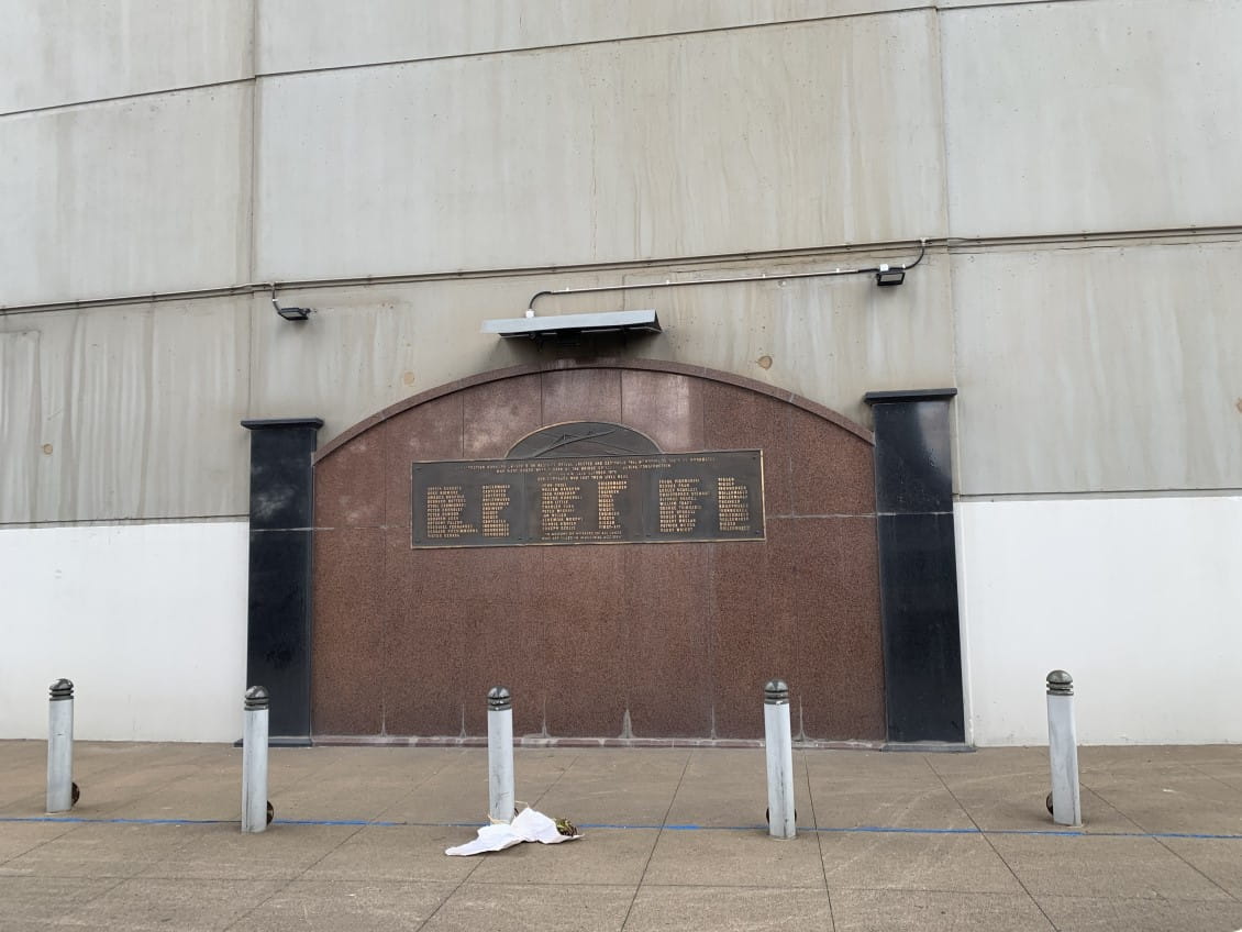 A wall, with a brass plaque with the names of the 31 workers who died in the Westgate Bridge disaster of 1970. A bouquet of flowers has been laid in front of it.