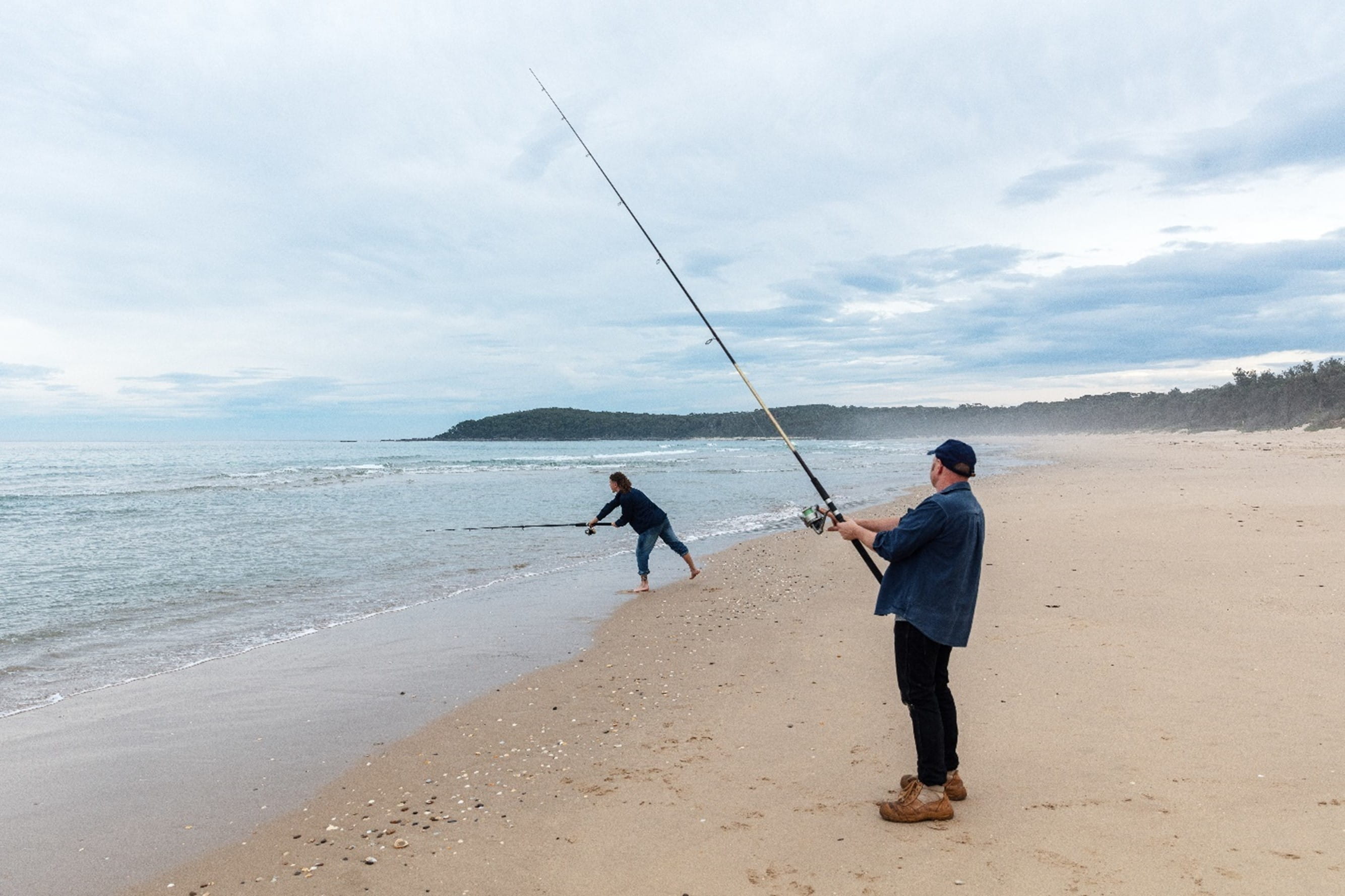 Two people fishing on the beach with fishing rods