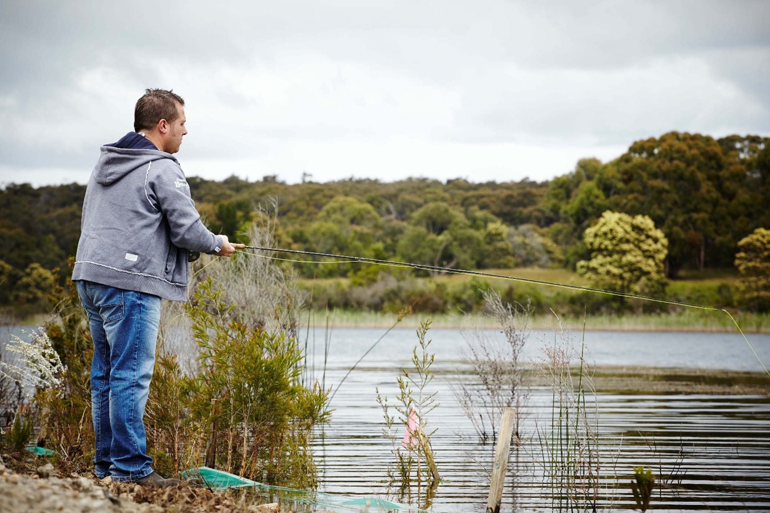 A person fishing near reeds and water