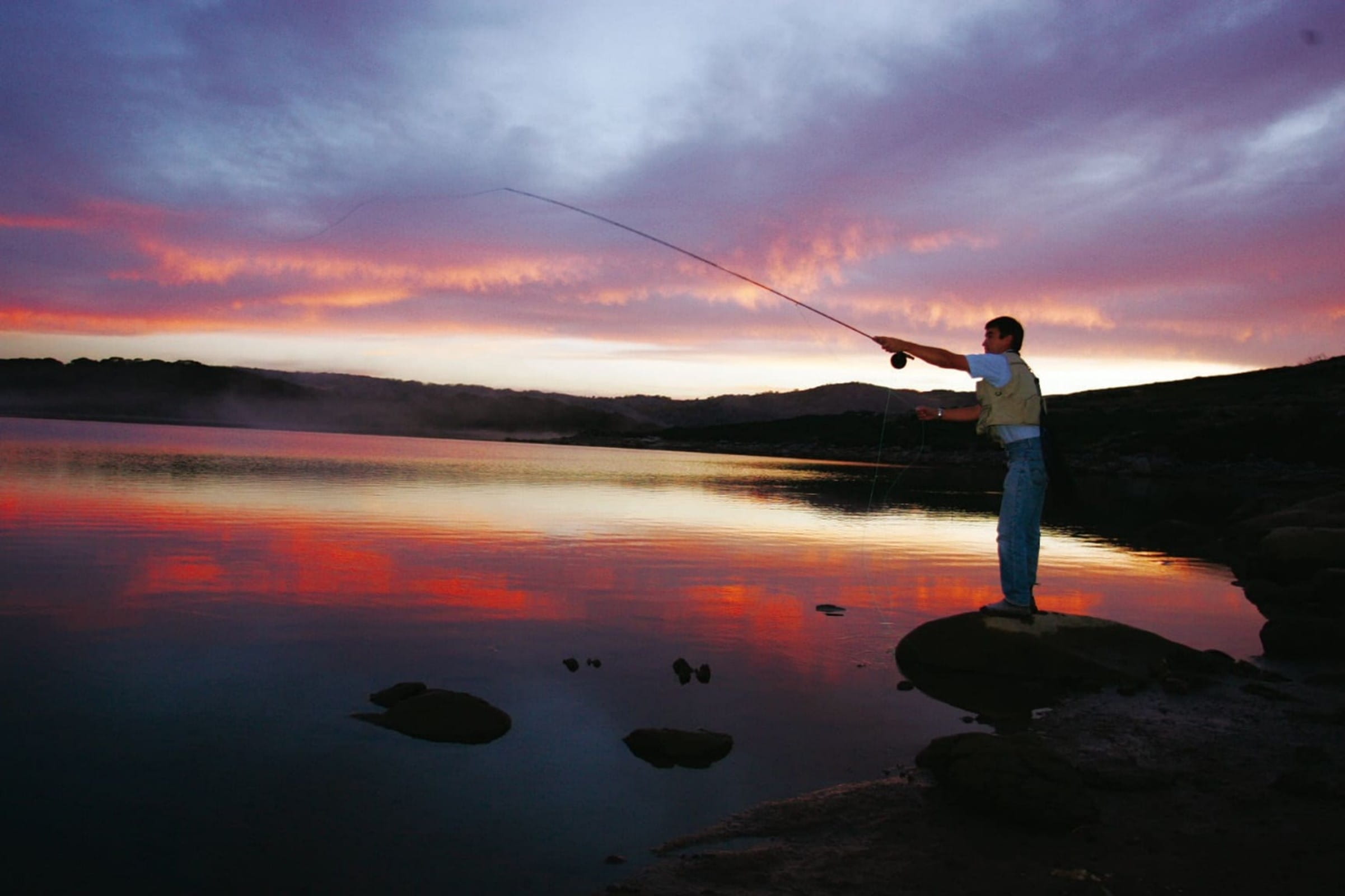 A person fly fishing with the sunset in the background