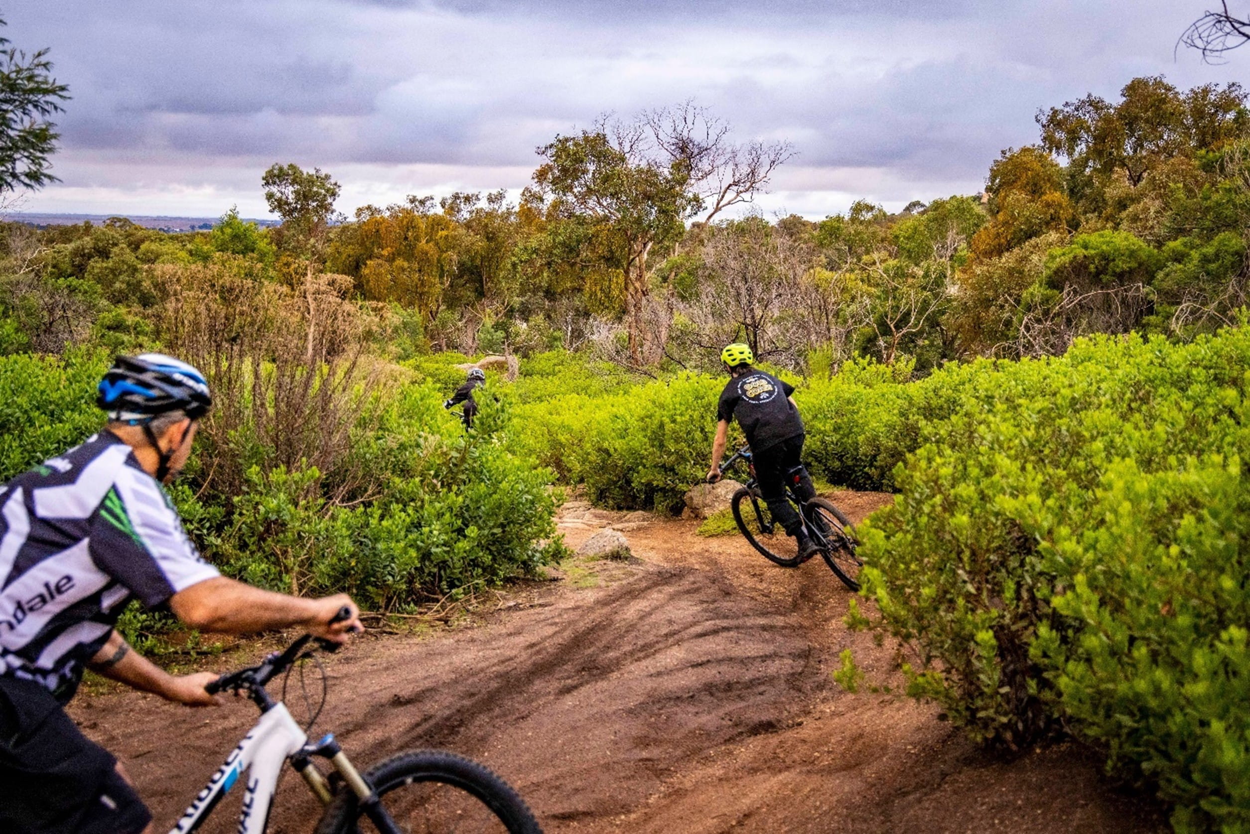 Two people are riding their bikes on a dirt path