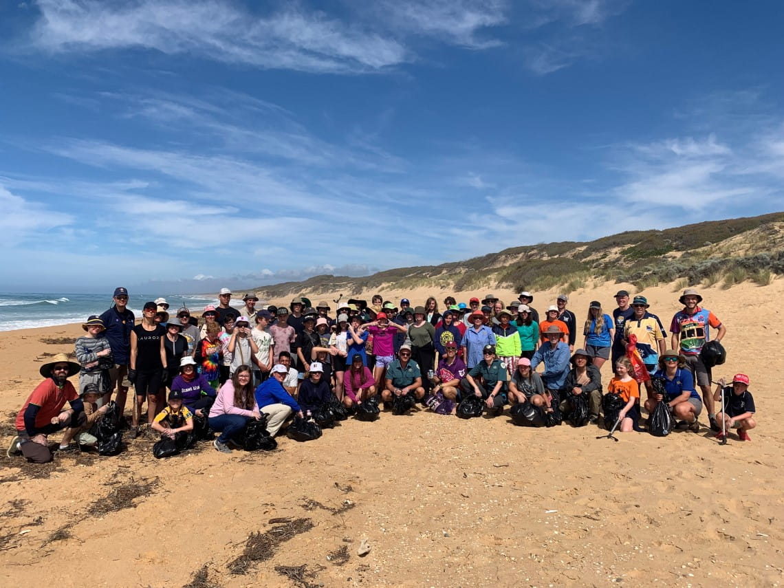 A large group of scouts standing and sitting on the beach smiling to the camera