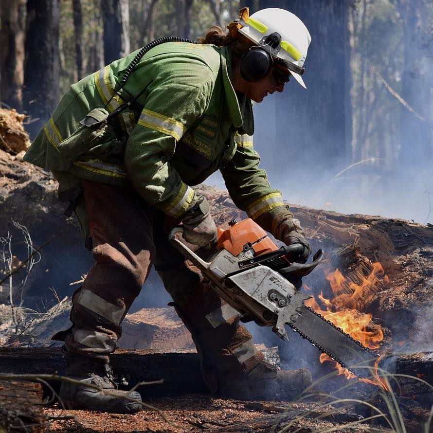 Joy in her firefighting gear, using a chainsaw to cut a burning log