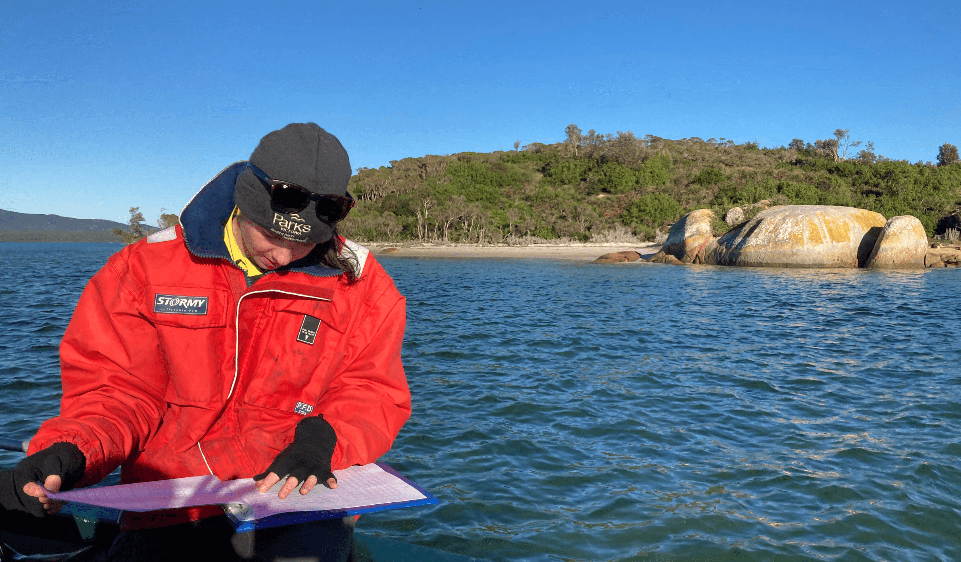 Cassidy sitting in a boat, looking at paperwork and undertaking marine monitoring