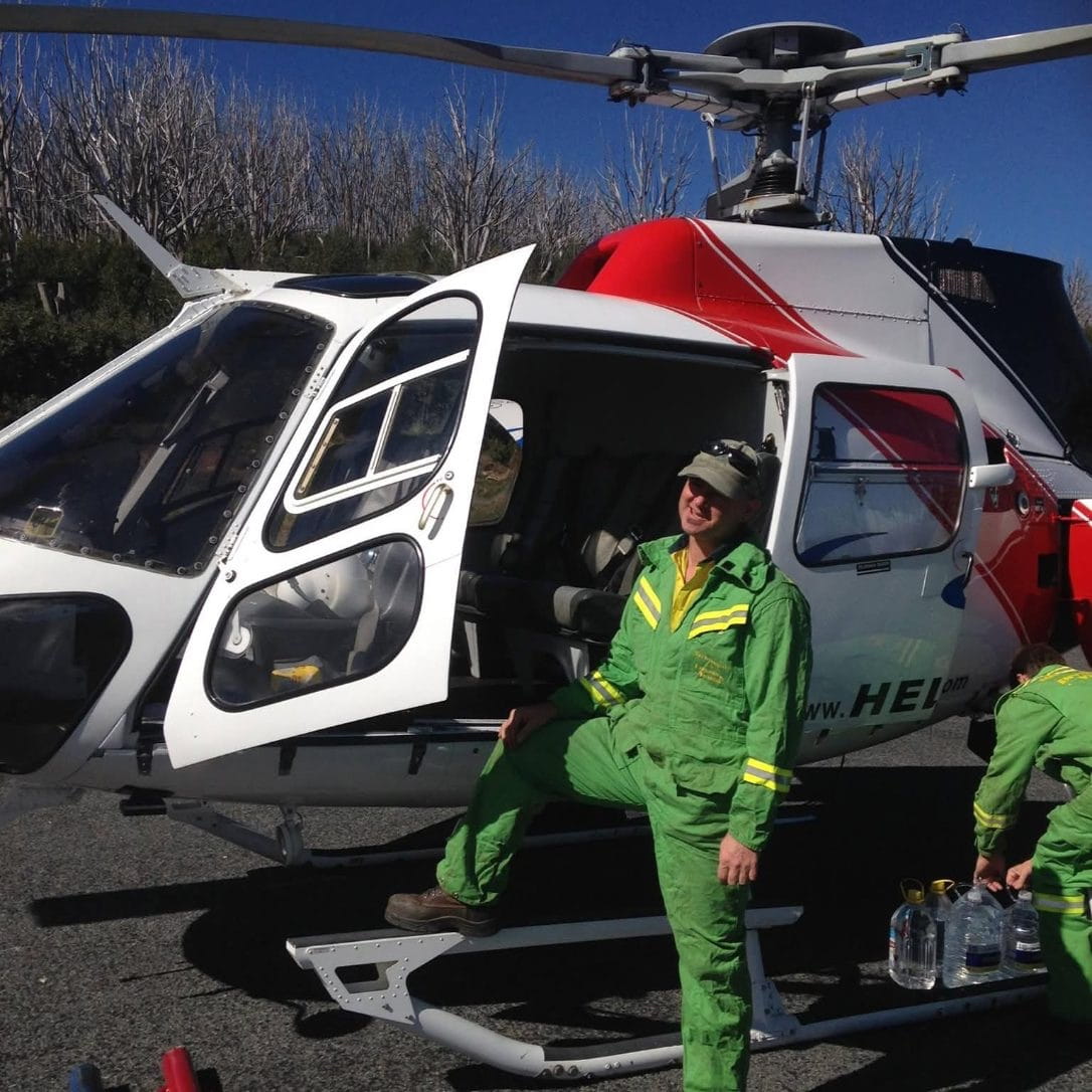 Man posing as he climbs out of a helicopter, dressed in hi-vis