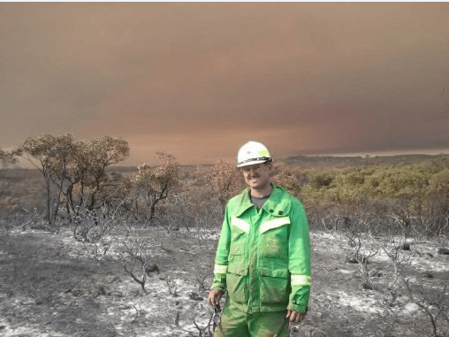 A man standing in hi-vis, taking a break from fire fighting in devastated country.