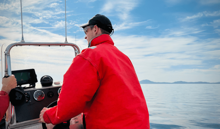 Ranger in hi-vis orange driving a boat