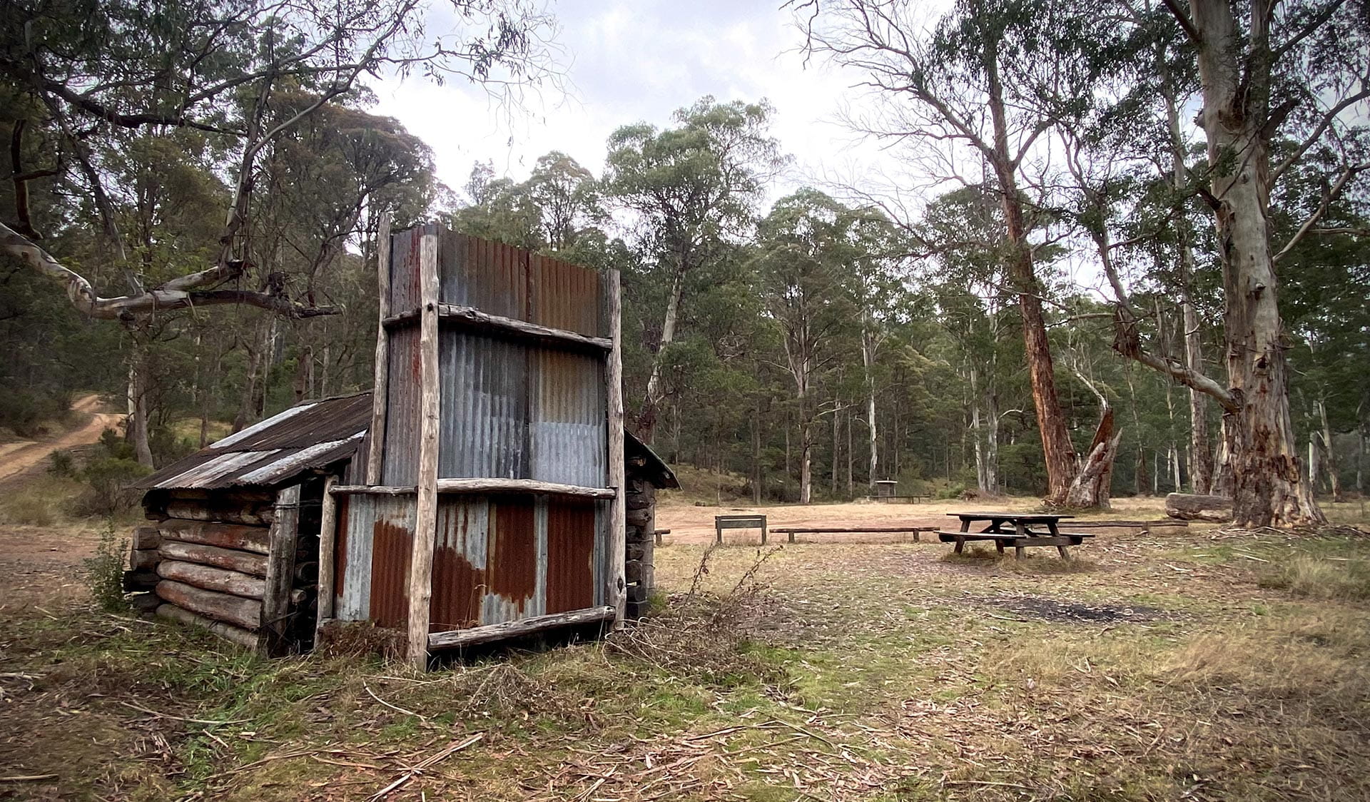 View of a hut and picnic table and bench in a camping area.