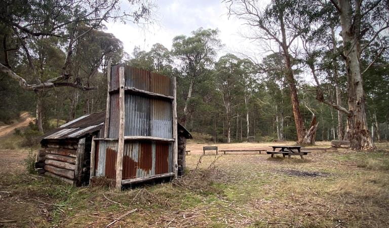 View of a hut and picnic table and bench in a camping area.