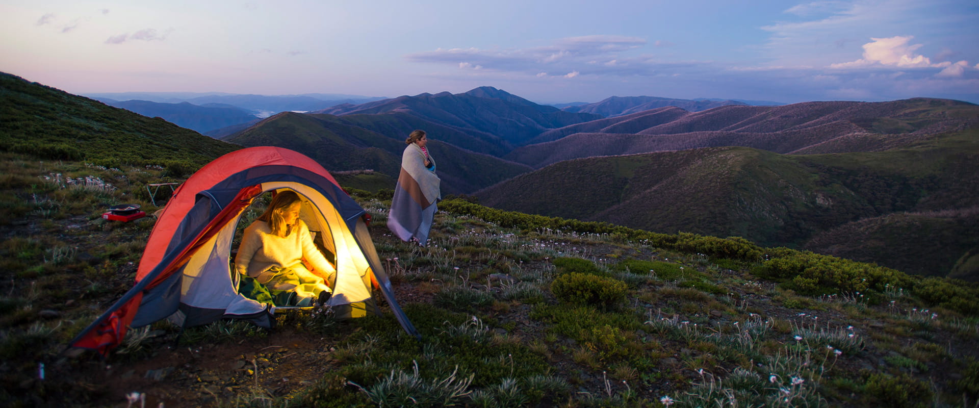Two hikers relax at their campsite that is high up on the mountain and enjoy surrounding  views