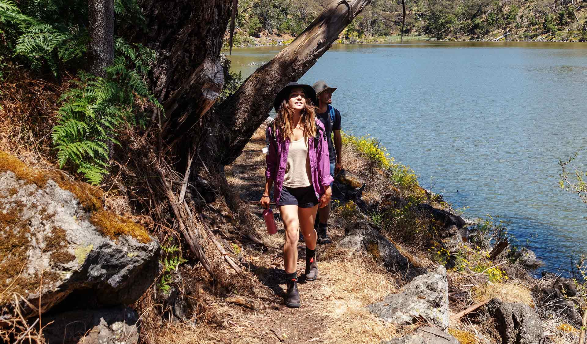 A young women leads a man on a walk along a river bank.