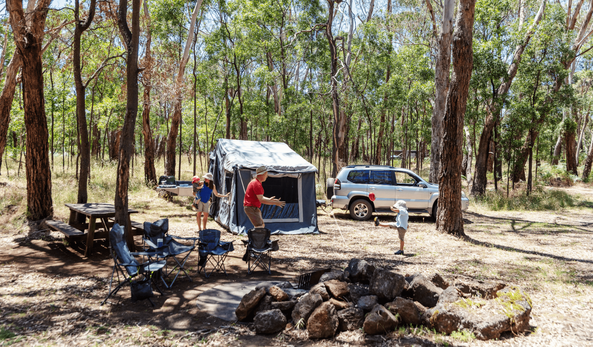 A father kicks a football with his young son infront of a trailer camper.