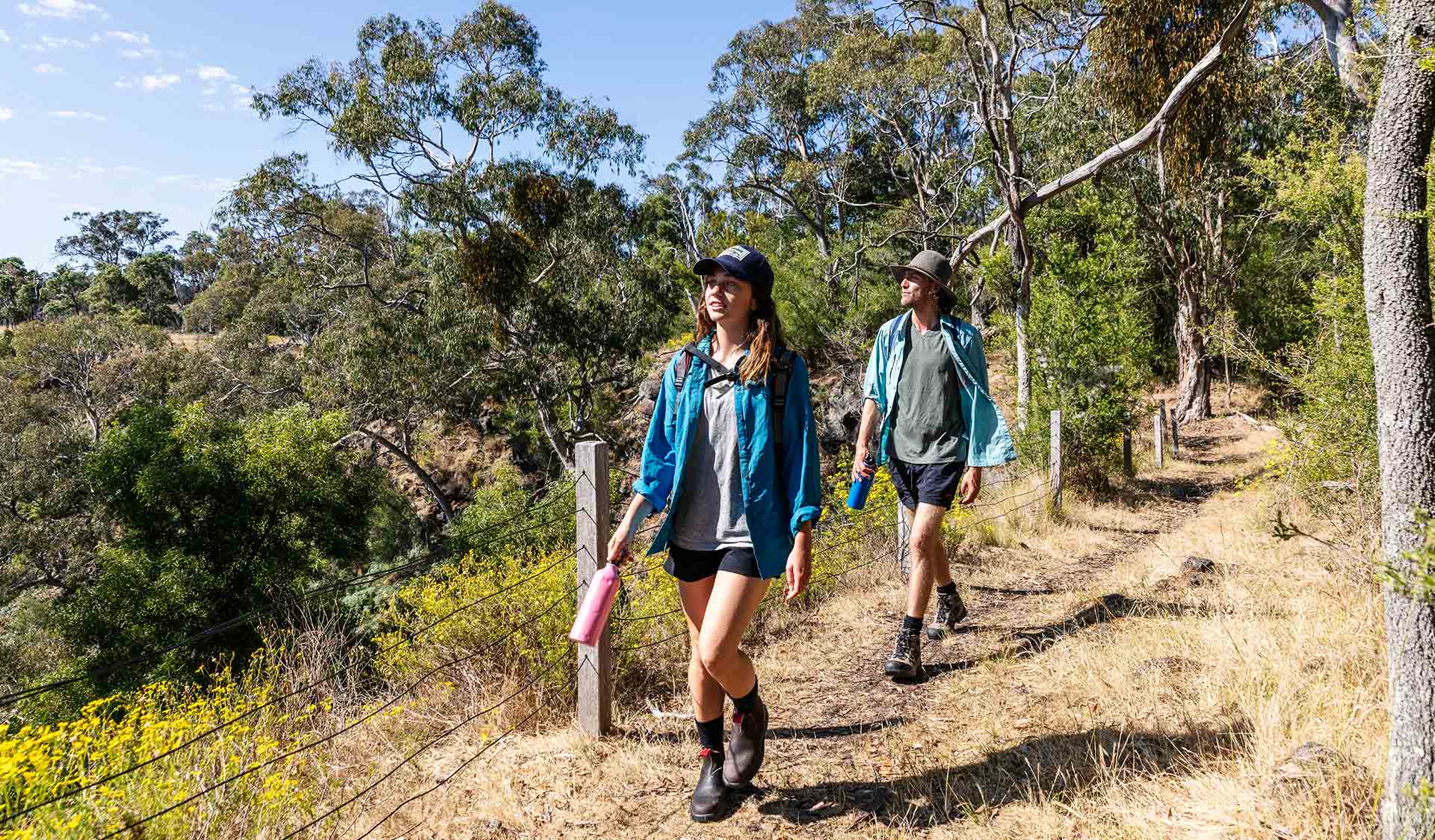 A young woman leading a man on a walk along a fenced grass path