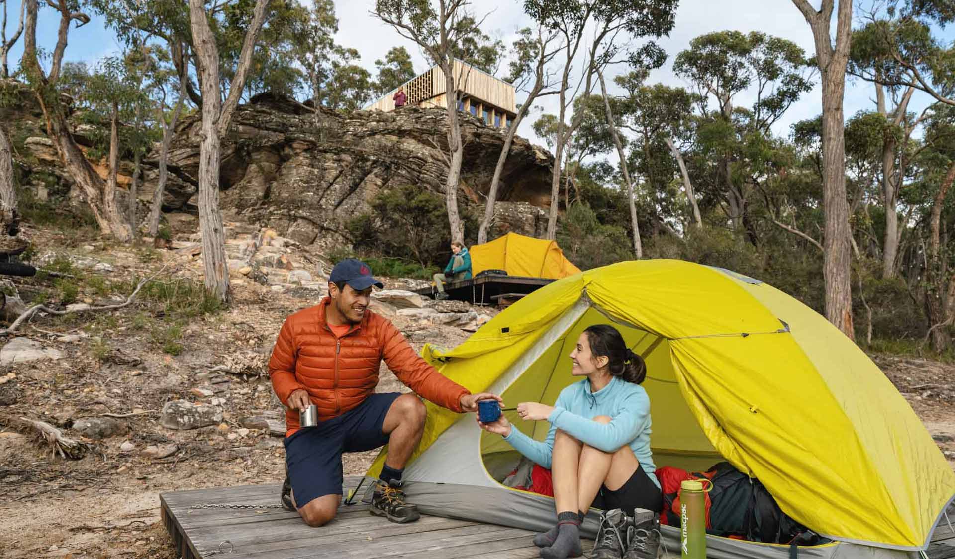 A man passes a cup of tea to his partner at their tent set up below the communal shelter at Djardji-Djawara Hiker camp on southern section 2 of the GPT