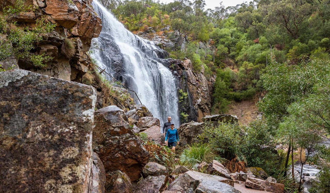 Two people walking along the path in front of Mackenzie Falls at Grampians National Park