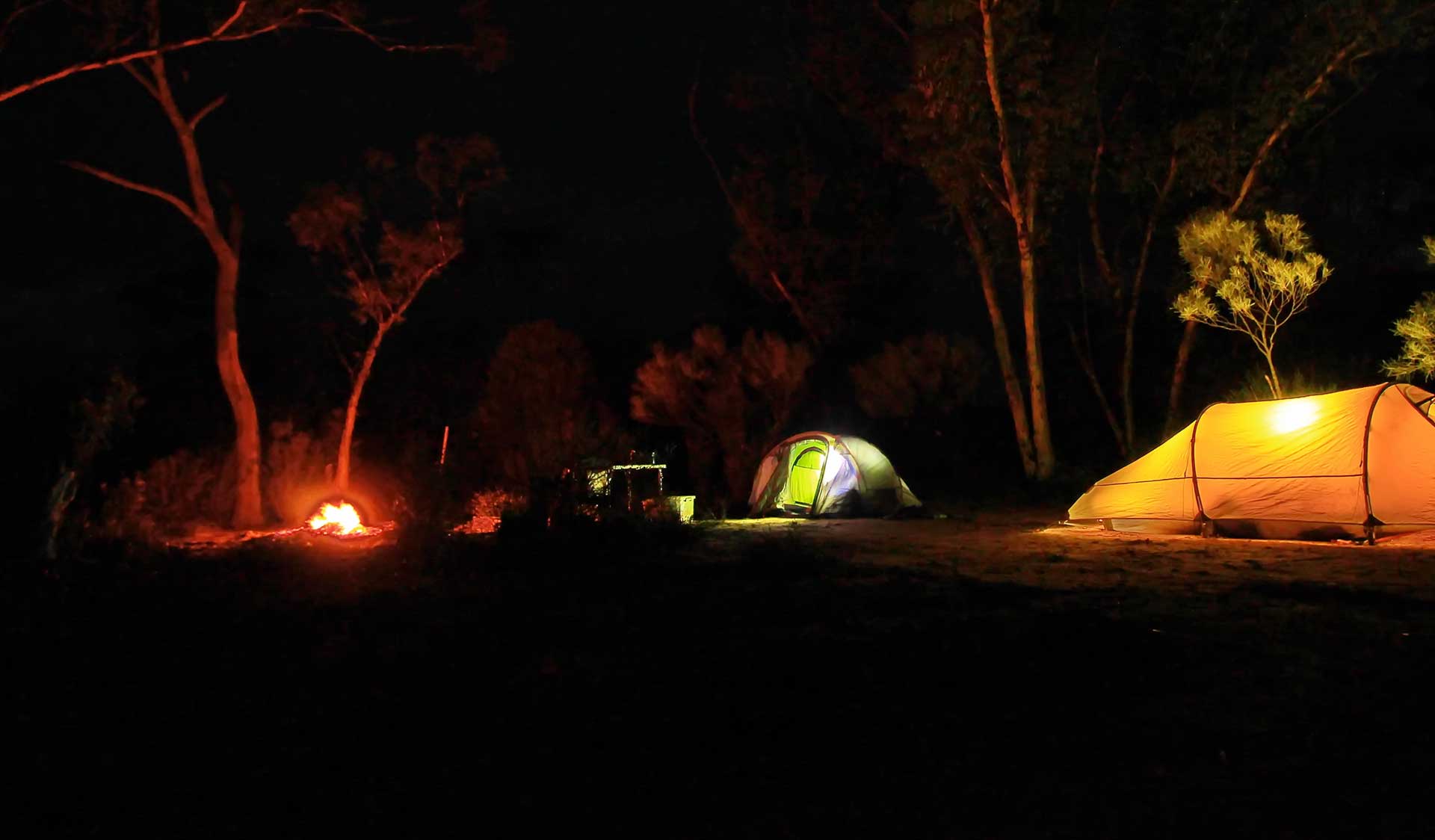 Three tents and a campfire at night time. 