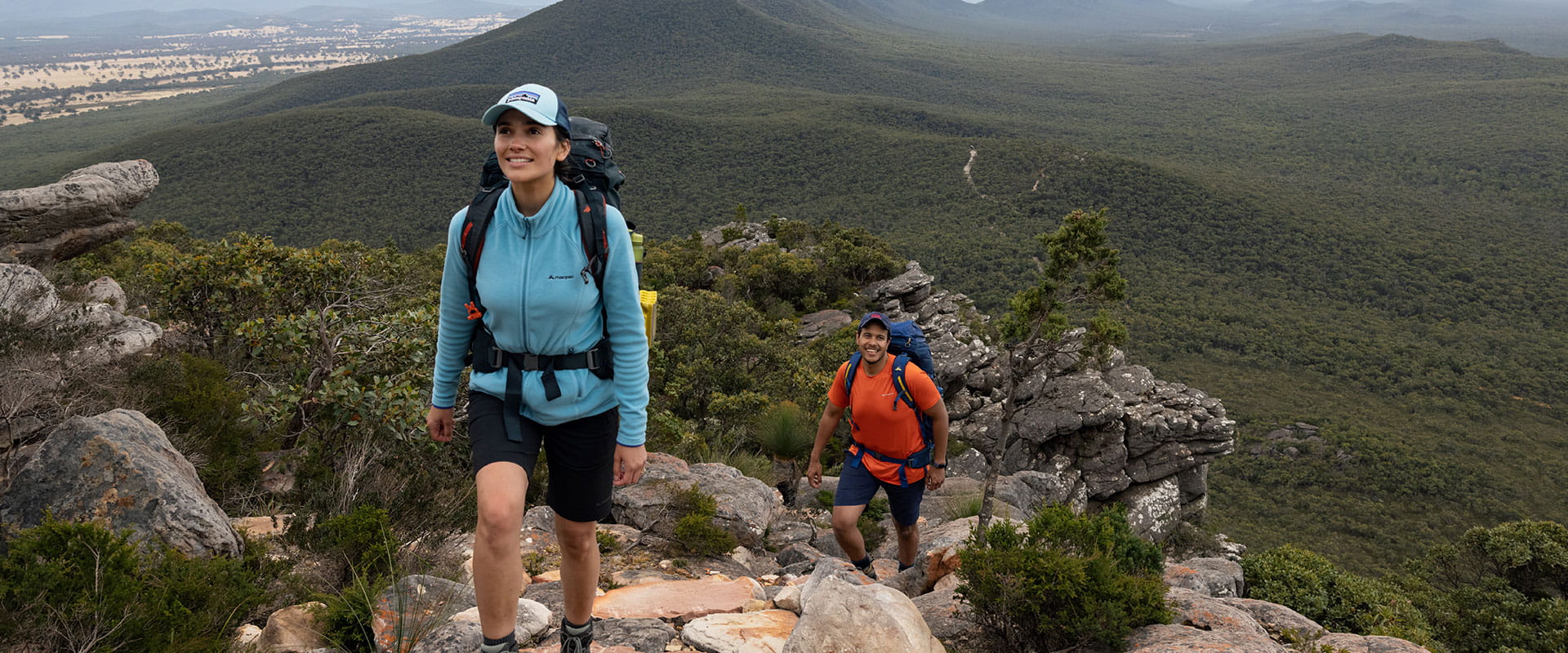Two hikers ascend a rocky staircase with big mountains views behind them
