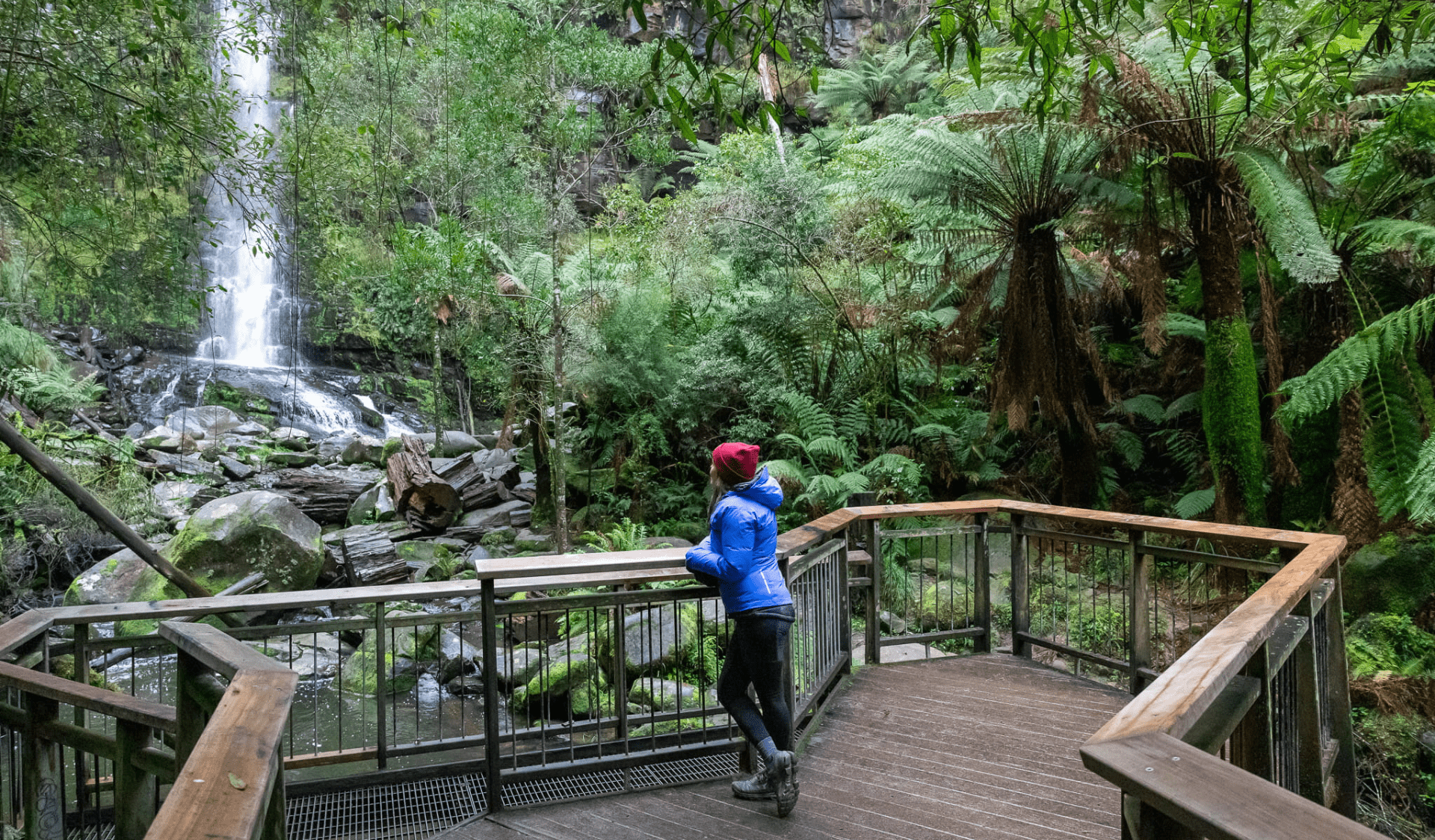 Person standing on viewing platform looking towards waterfall.