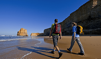 A couple with pack walk along the beach toward the Twelve Apostles