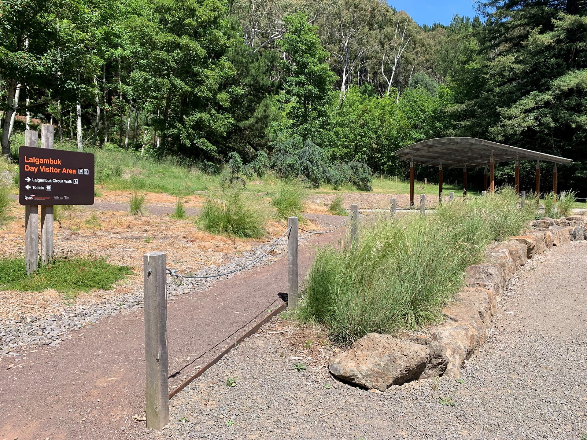 A sign on the left reads Lalgambuk Day Visitor Area at a path leading to a shelter with trees in the background.