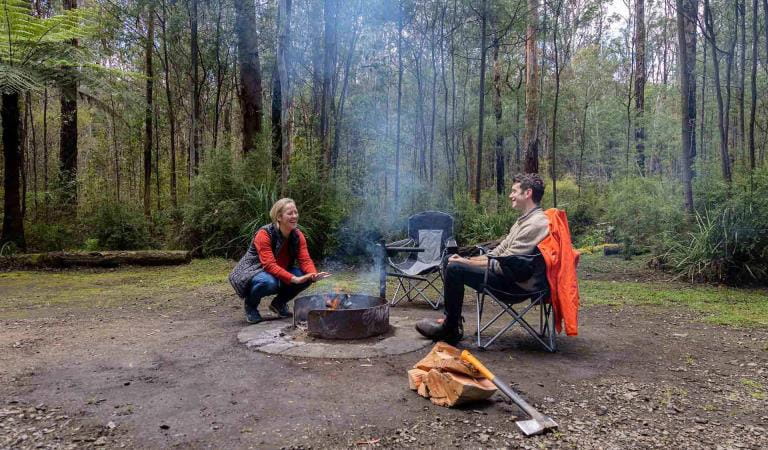 A man and women sit beside a fire at the Gums Campground at Kinglake National Park