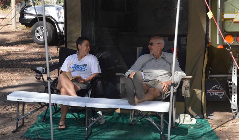 Two friends relax under the shelter of their camper trailer at Fraser Camping Area in the Lake Eildon National Park.