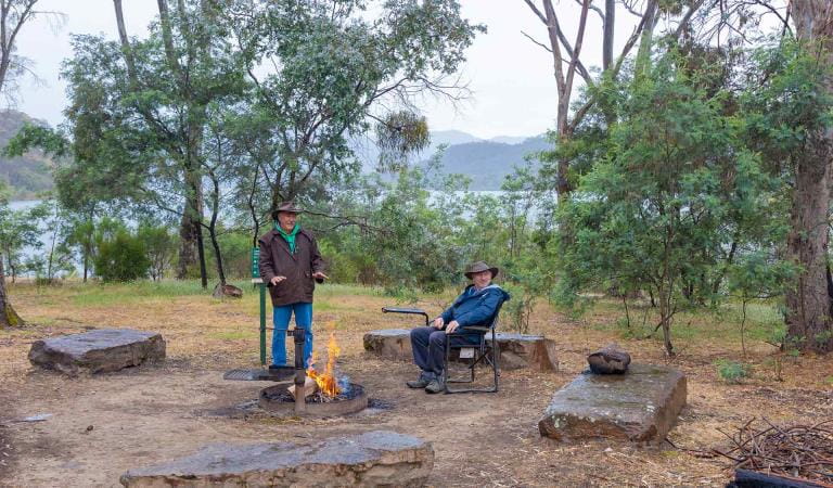 Two men warm up next to a campfire at Devil Cove Campground at Lake Eildon National Park