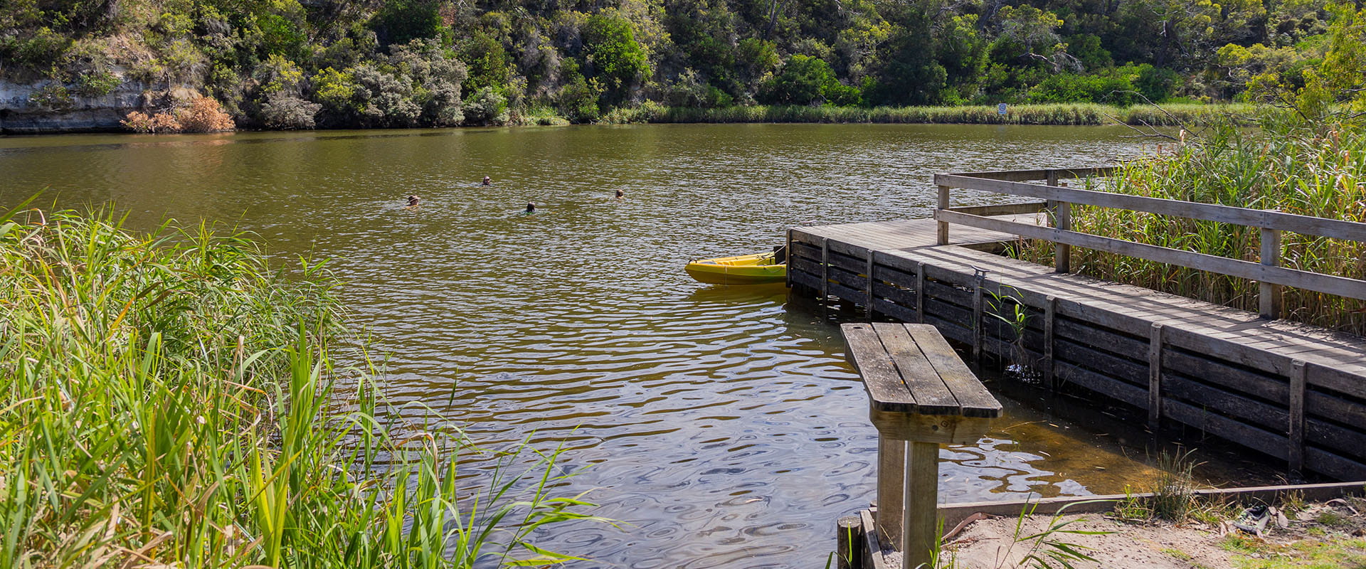 People swimming in a lake. A small wooden jetty in the foreground. 