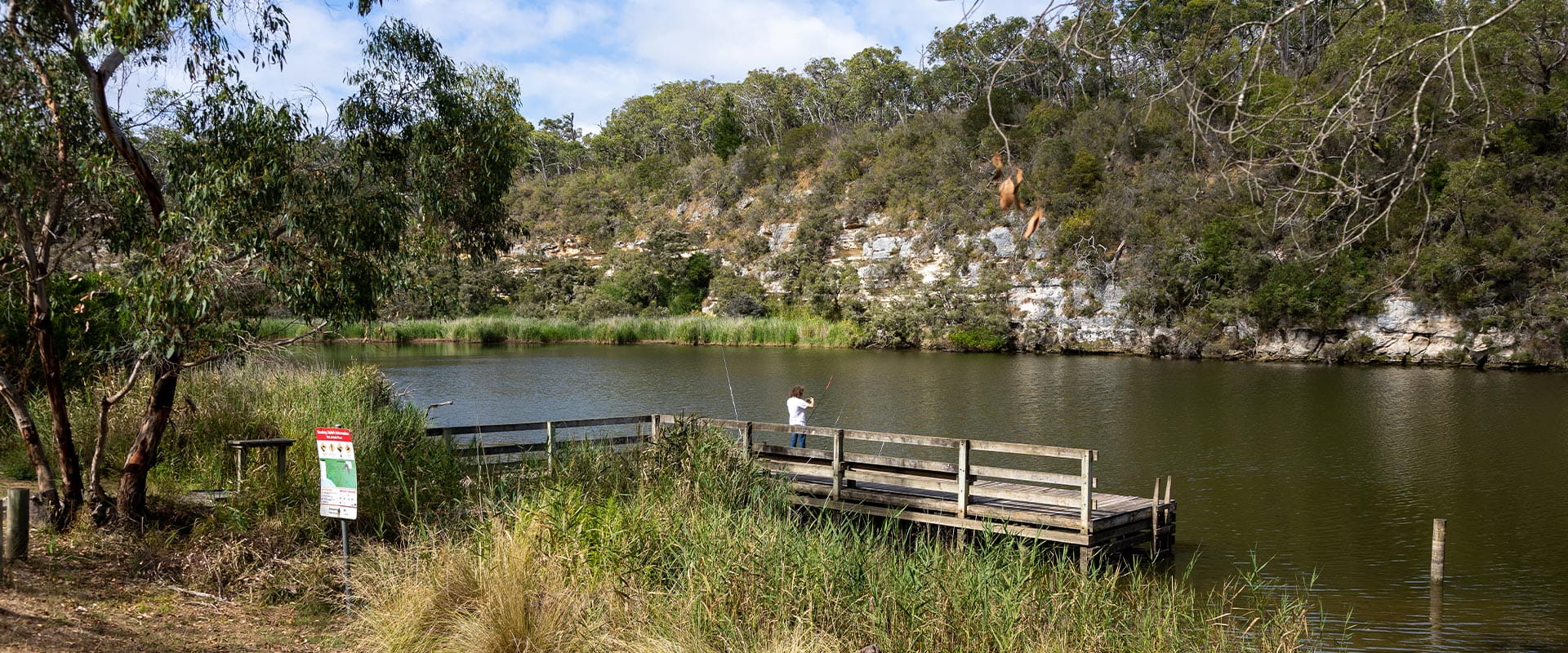 A man fishes in the Glenelg River off a wooden punt.