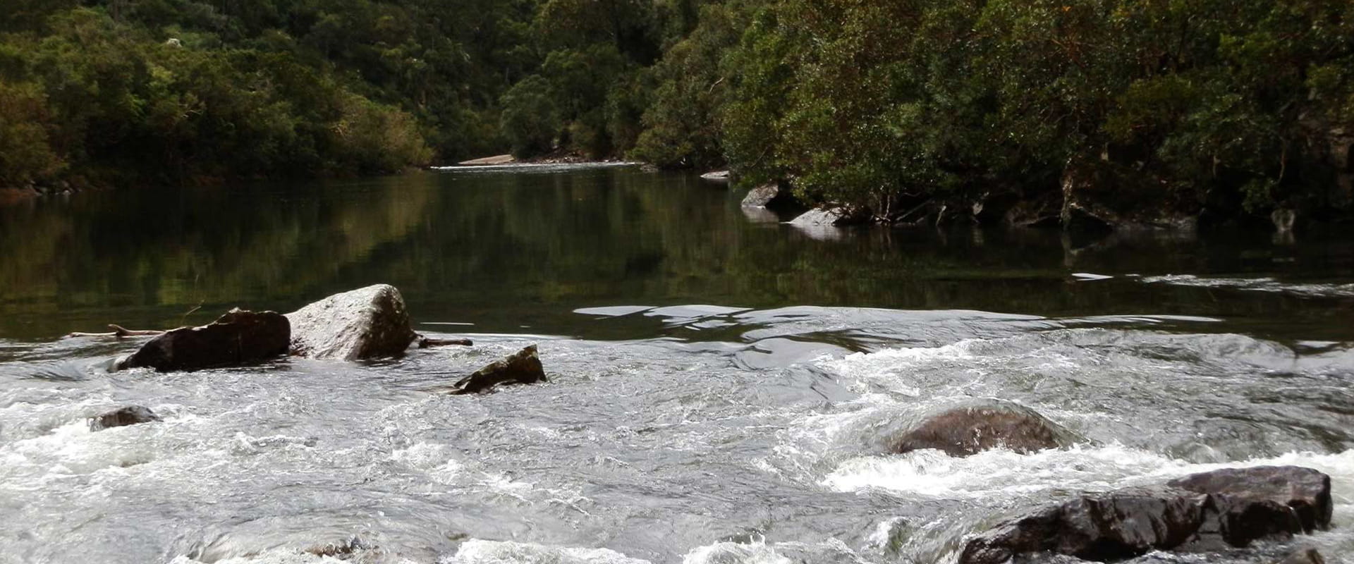 A large river flows through green rugged bushland