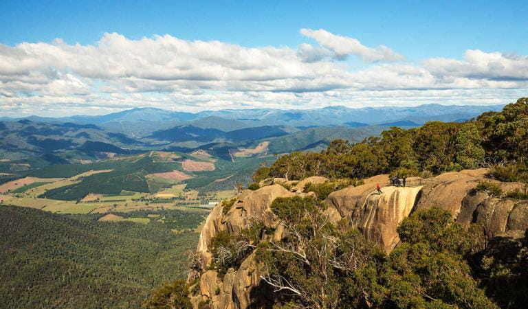 A group of abseilers descend into the Gorge at Mt Buffalo with views of the Bogong High Plains in the back ground.