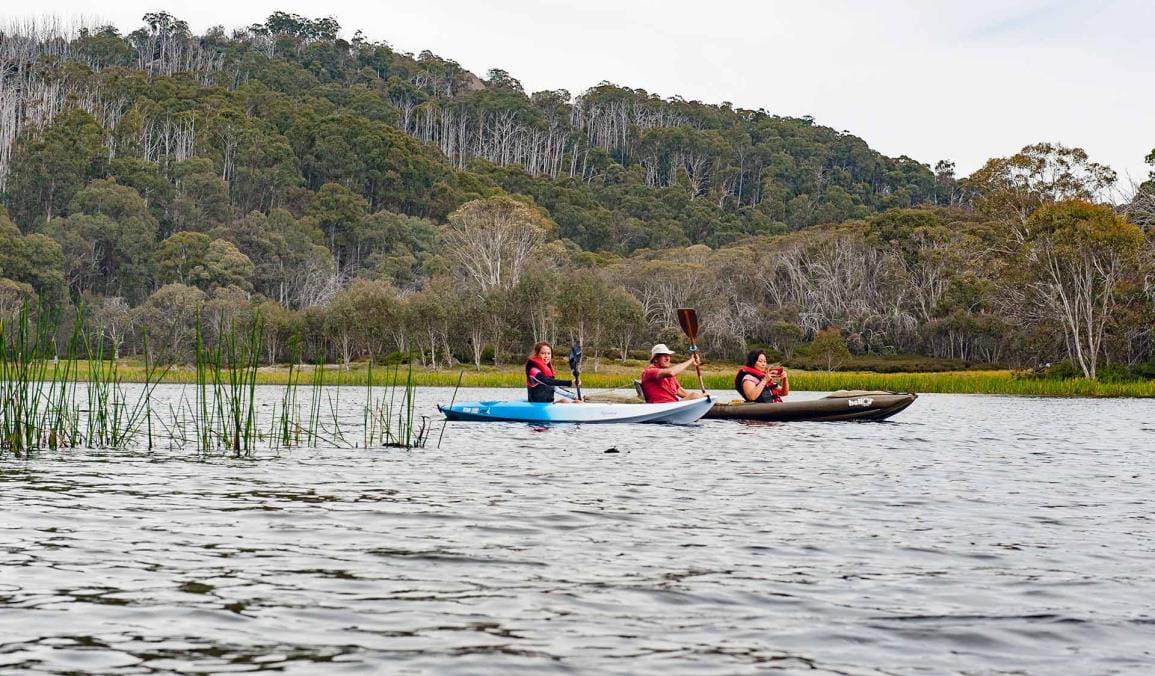 Three friends kayak across the waters of Mount Buffalo's Lake Catani.