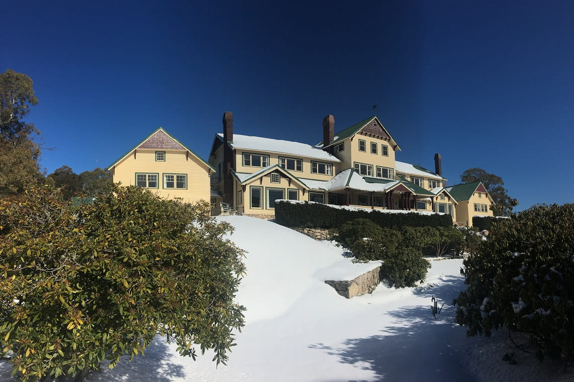 A wide lens photo of the Mount Buffalo Chalet. A blanket of snow covers the gable rooves of the Chalet and the surrounding garden.
