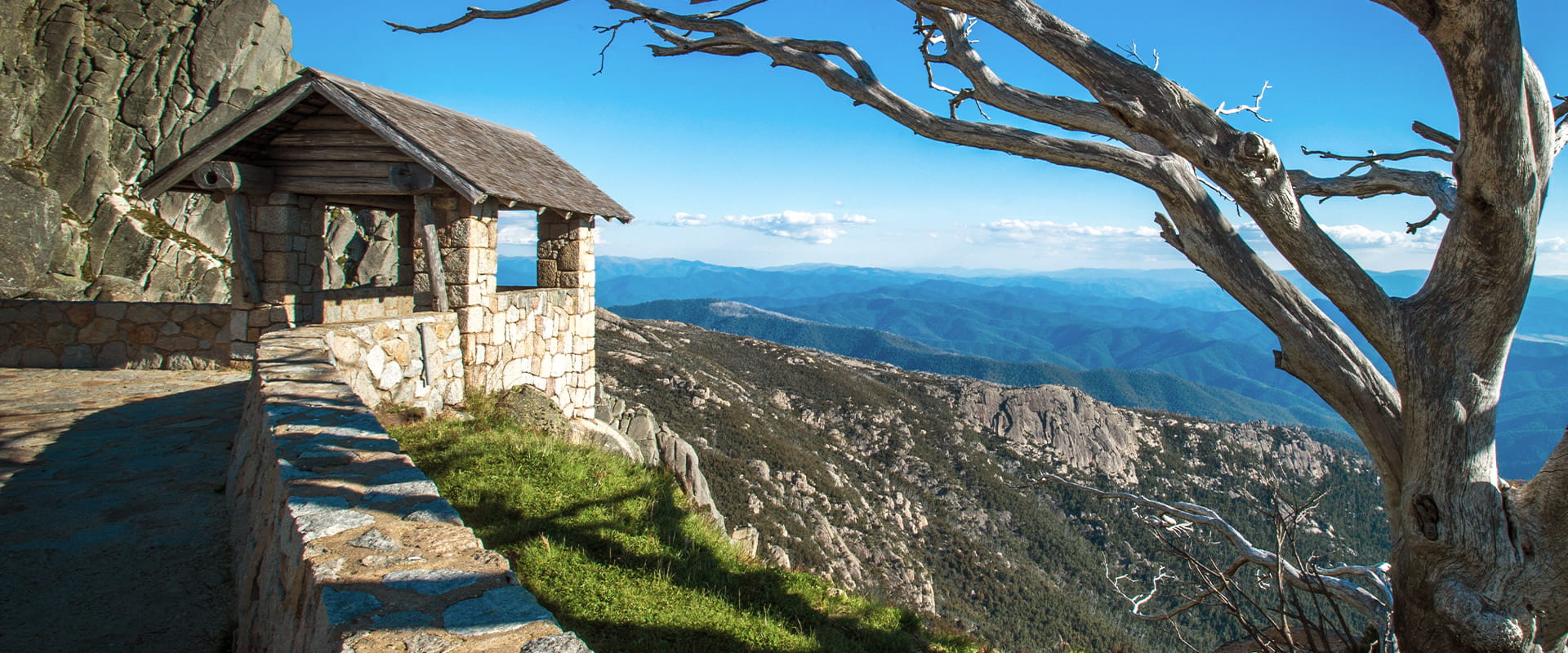 A stone hut overlooking an alpine view framed by a ghostly snowgum