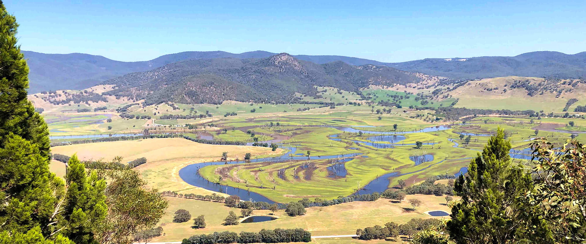 A winding river flows amongst surrounding hills. The river breaks off into multiple streams across a floodplain.