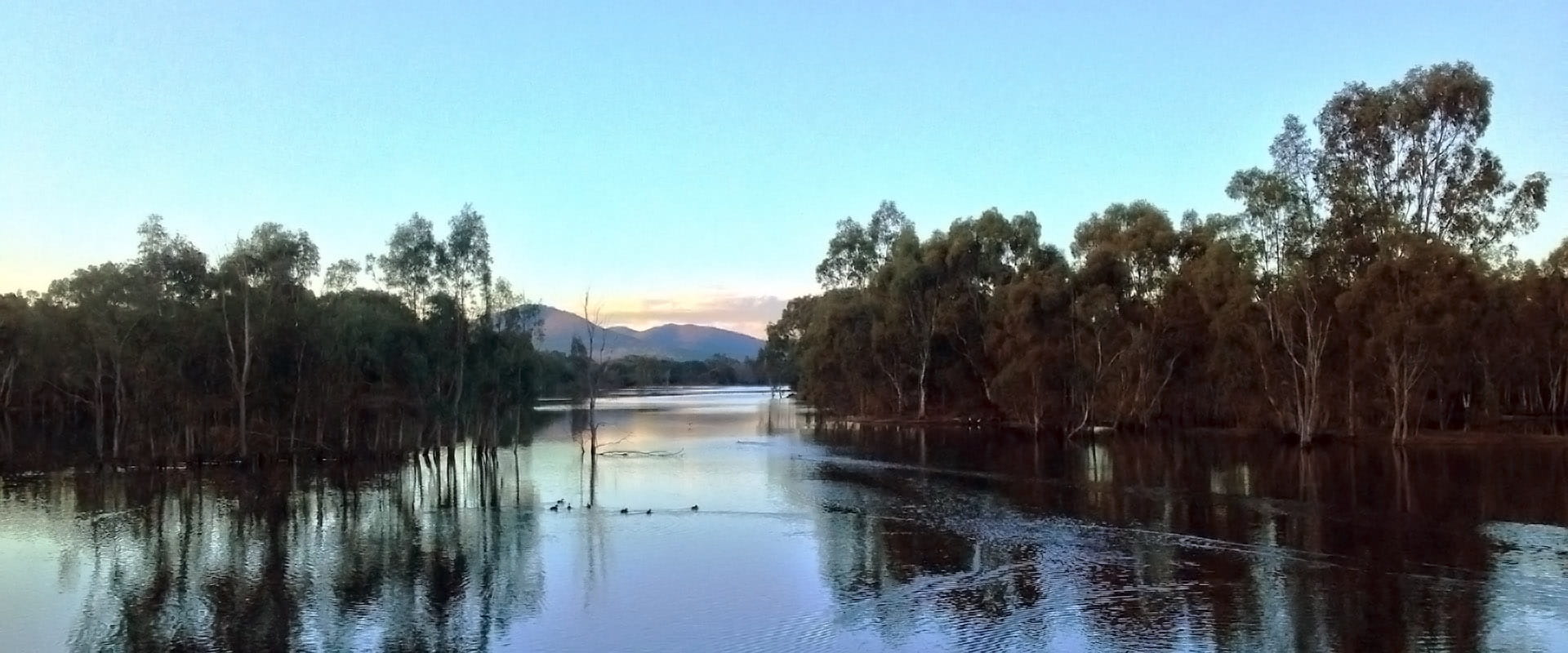 A blue lake just before the sun rises up over rocky hills in the background