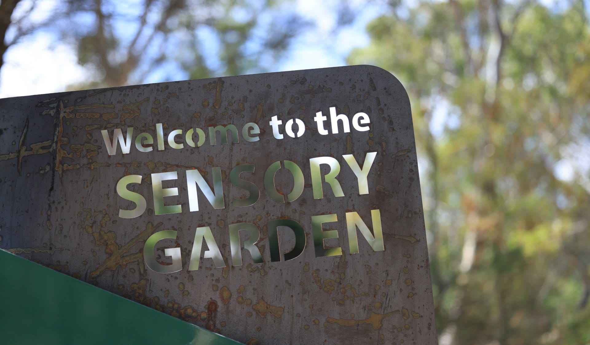 Photo of a rusted steel sign at the entrance of the Sensory Garden that says ‘Welcome to the Sensory Garden’. 