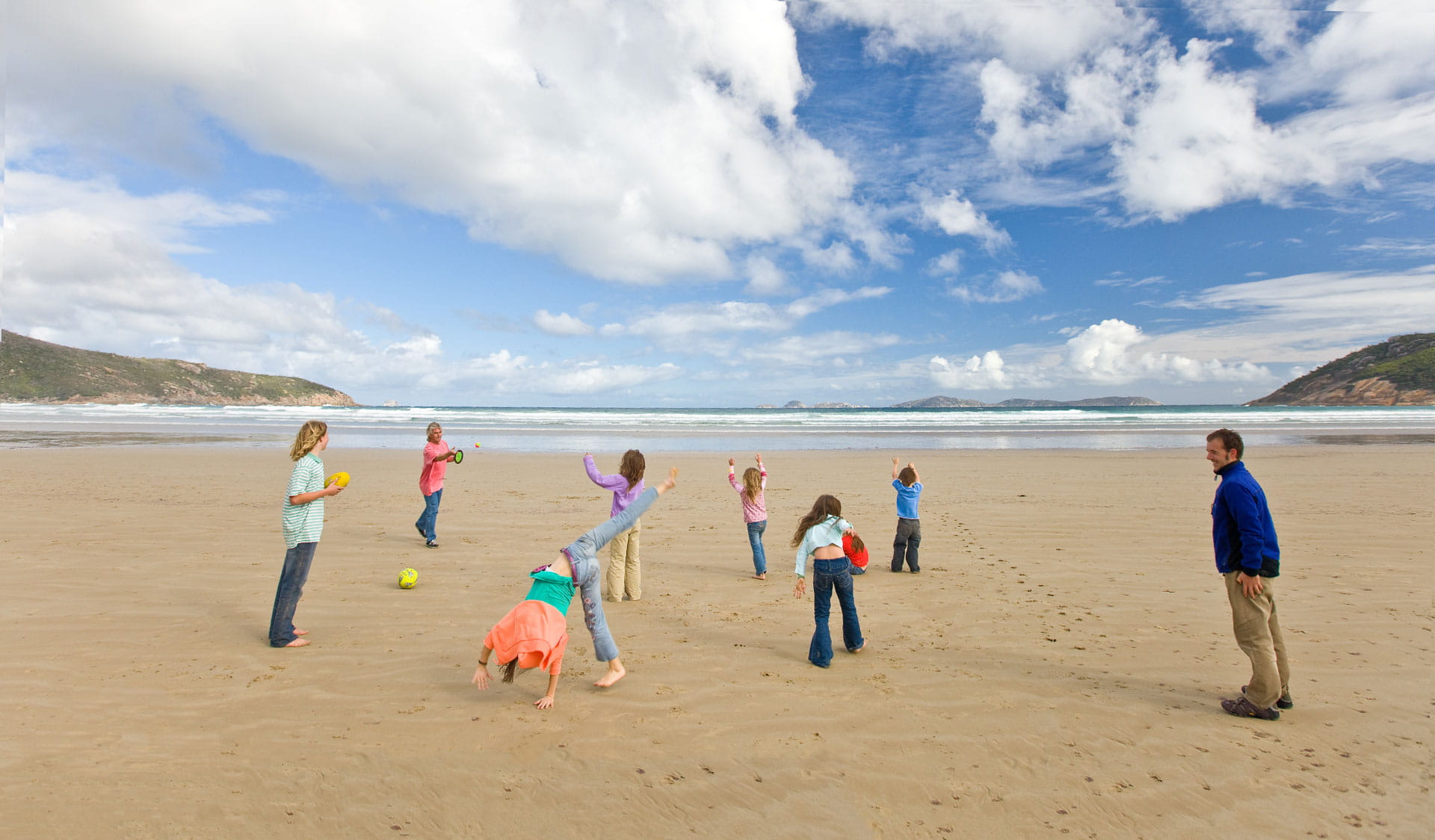 An extended family play with a couple of balls on squeaky beach.