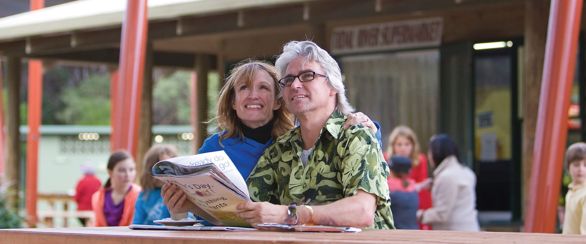 A couple sit at a table reading the paper outside of the Visitor Centre
