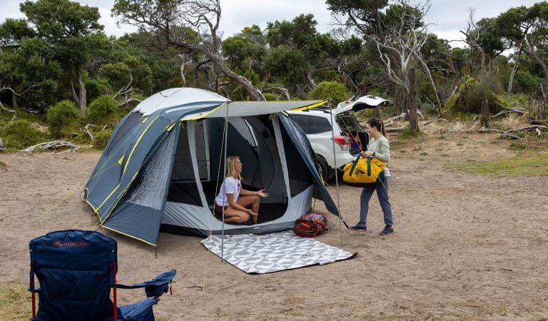 Two women setting up their camping space on sand.