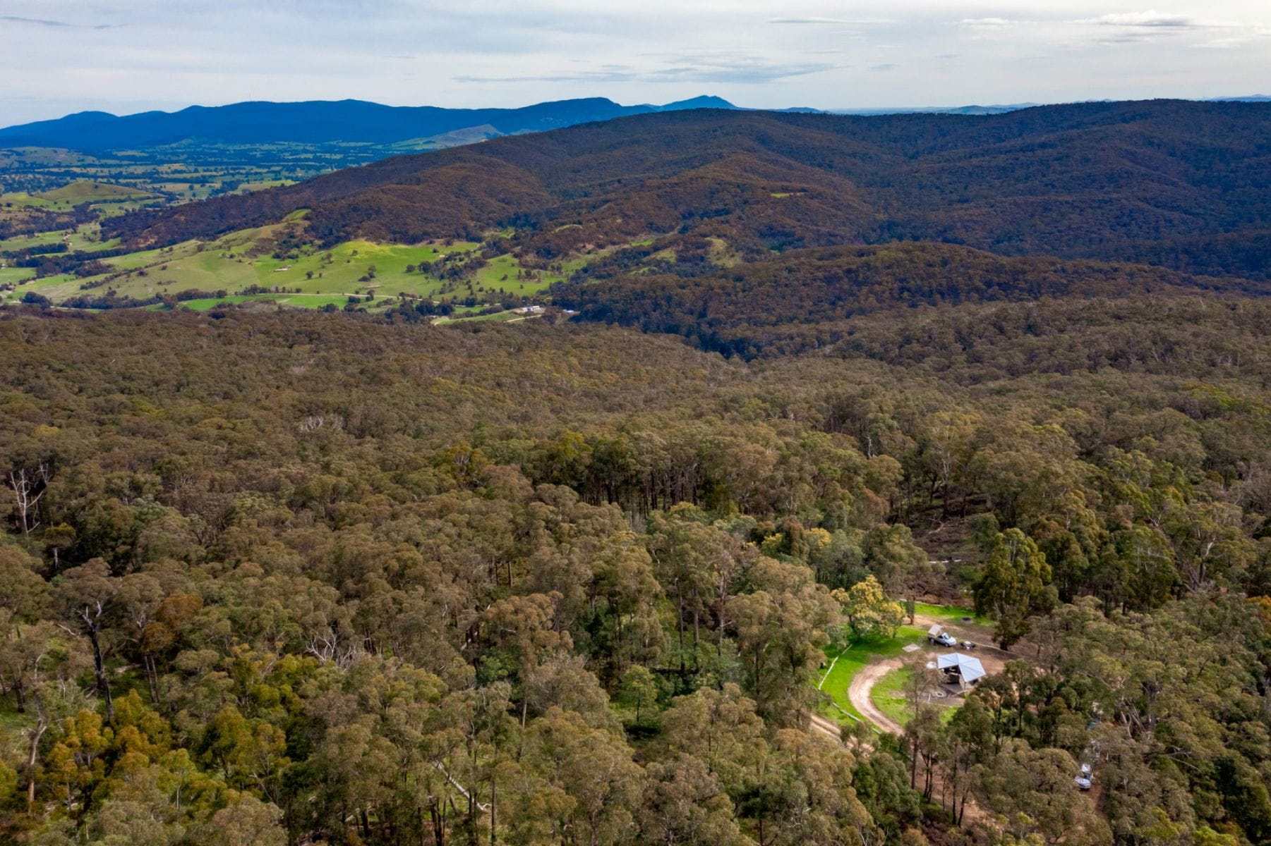 A view of bushland from above showing a clearing with a campground on it. 